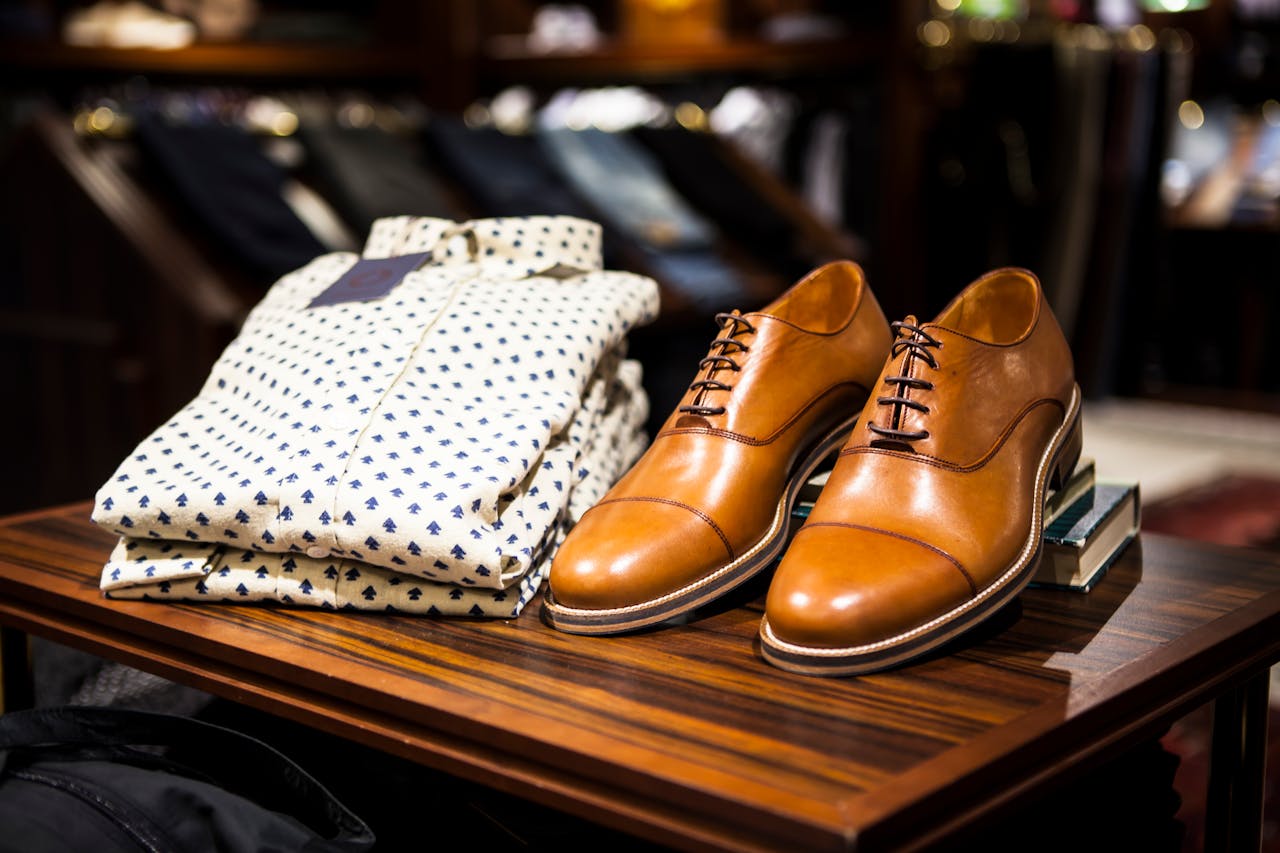 home-hero Elegant brown leather shoes and printed shirt displayed on a wooden table in a stylish clothing store.